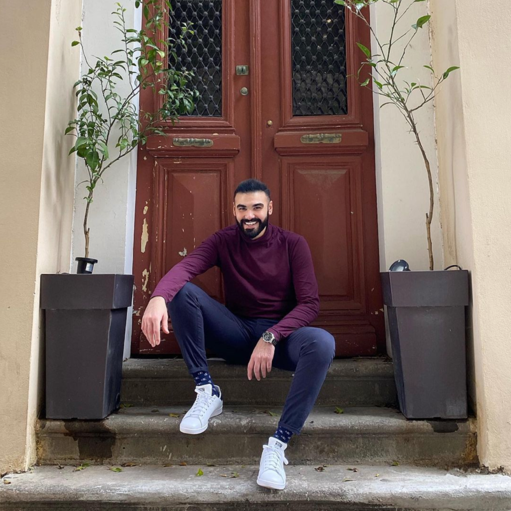 Theodoros Kalotinis sitting on steps in front of a door, smiling at the camera.