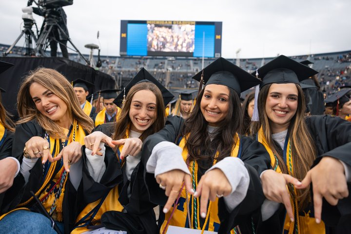 A group of people in caps and gowns at graduation making M's with their hands