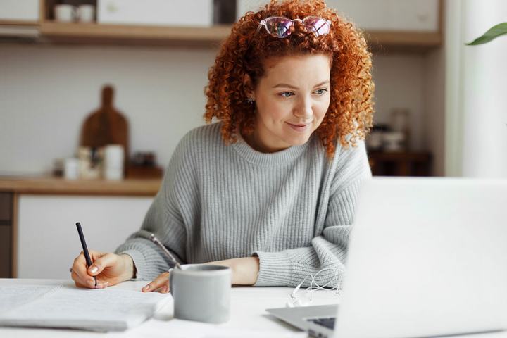 Woman taking notes while looking at a laptop